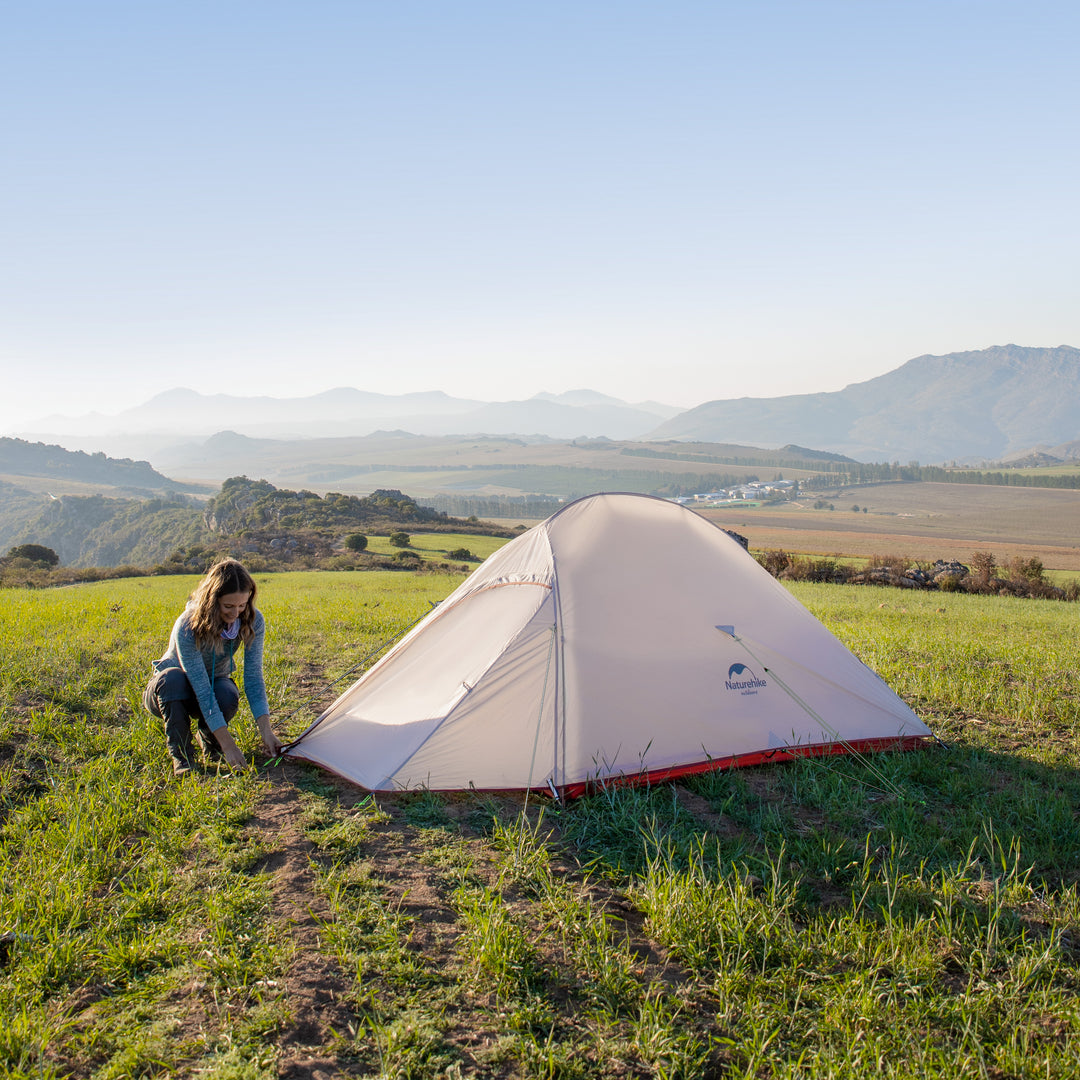 A woman setting up the Naturehike Cloud Up Pro 3-Person ultralight backpacking tent on a grass field, showing a sturdy, breathable, and easy-to-assemble design for comfortable camping and hiking.