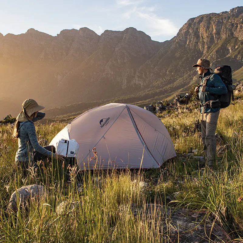Two hikers setting up the Naturehike Star-River 4-Season Backpacking Tent on a sunny day at the base of magnificent mountains. Illustrates the tent's suitability for high-altitude and scenic mountain camping.