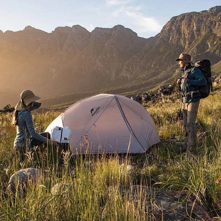 Two hikers setting up the Naturehike Star-River 4-Season Backpacking Tent on a sunny day at the base of magnificent mountains. Illustrates the tent's suitability for high-altitude and scenic mountain camping.