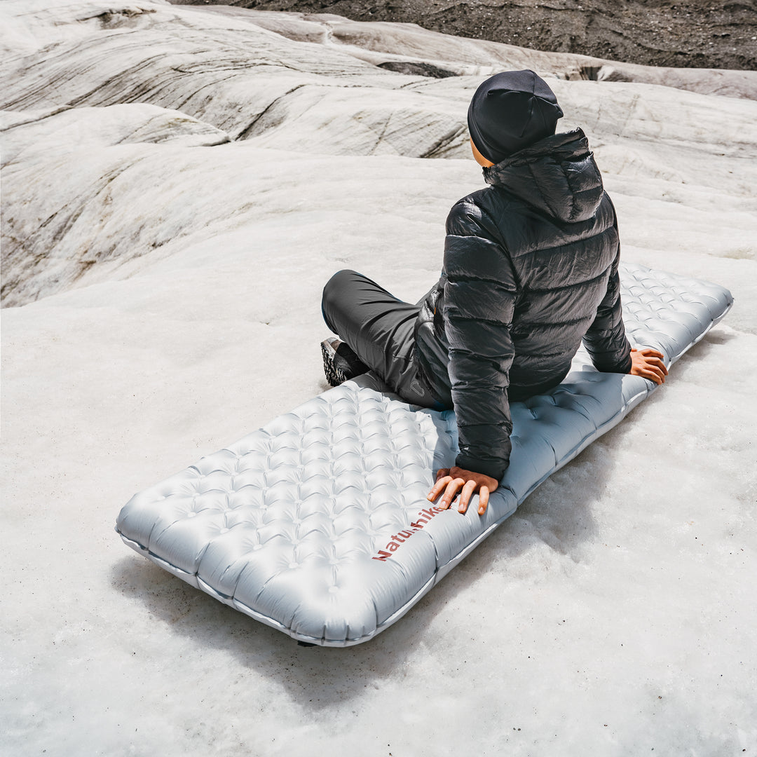 Naturehike TuYe ultralight inflatable sleeping pad used outdoors with a man sitting on the pad, showcasing comfort and support in real camping conditions, ideal for backpacking, hiking, and cold-weather adventures.