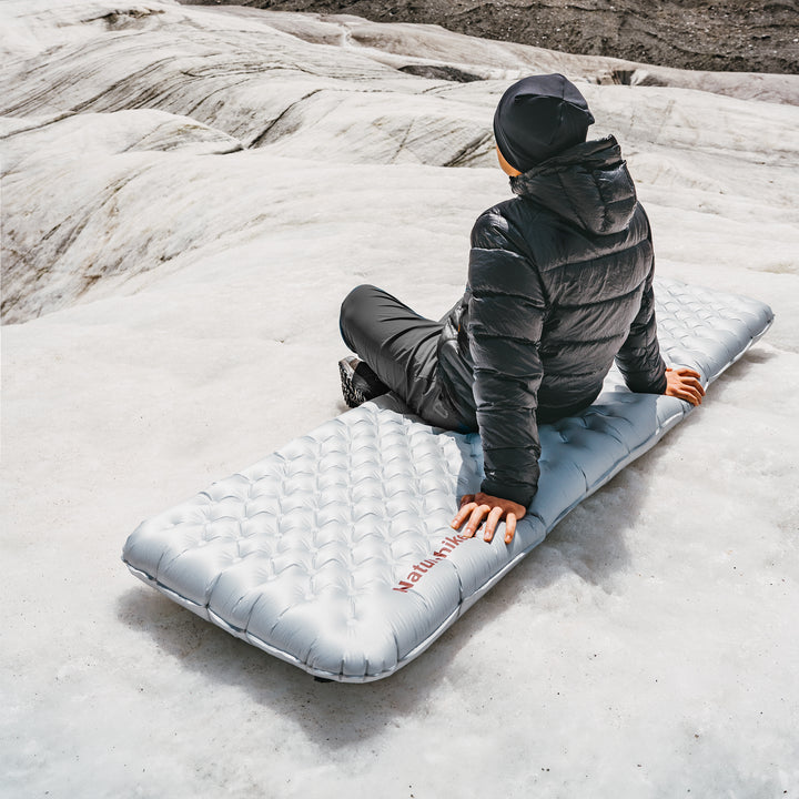 Naturehike TuYe ultralight inflatable sleeping pad used outdoors with a man sitting on the pad, showcasing comfort and support in real camping conditions, ideal for backpacking, hiking, and cold-weather adventures.